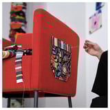 A person sits at a red upholstered desk with fabric decorations and a striped ribbon.