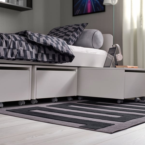 Cozy bedroom with striped bed, built-in drawers, gray rug, and pink-trimmed ottoman.