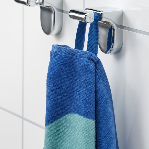 A blue and green striped towel hangs on a chrome bathroom hook. The hook securely fastens the towel, keeping it within easy reach.