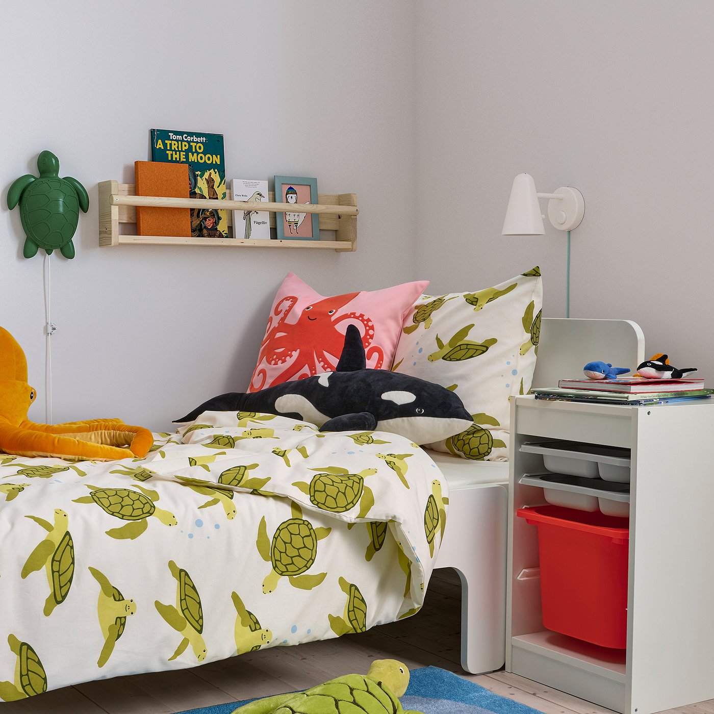 Childs bedroom with BLÅVINGAD turtle-patterned bed, bookshelf, lamp, red basket, whale pillow, turtle rug. Cozy and perfect for a young child.