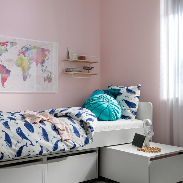 A cozy bedroom with a BLÅVINGAD duvet cover in blue whale design on a bed, featuring a turquoise pillow and a colorful world map on the wall.