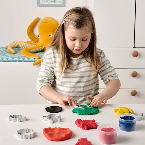 Girl plays with colorful modeling dough and cutters.