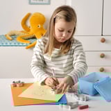 A girl uses cookie cutters and drawing on paper; a toy octopus sits nearby.