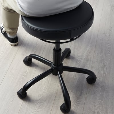 Person sitting on BLYKOBB active stool with leather seat, five-star base, and wheels.