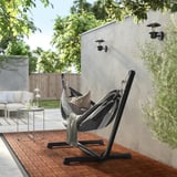 Relaxing garden scene with BOCKÖN hammock. Black stand, grey hammock, cushioned for comfort. Surrounded by plants and patio furniture.