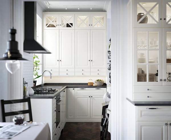 Modern white kitchen with off-white cabinets, gray countertop, stainless sink, black hood, and glass cupboards.