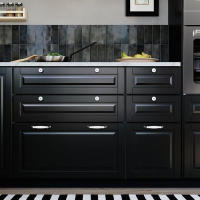 Modern kitchen with BODBYN black cabinets, marble countertop, green vegetables, and stainless steel appliances.