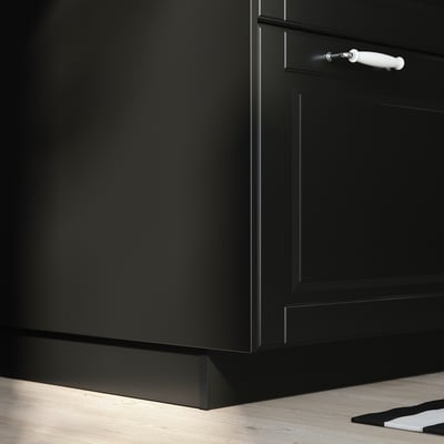 Black kitchen cabinet with white handle on wooden floor.