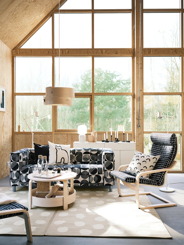 Modern living room with large windows, wooden decor, and black & white BOGENSE rug. An l-shaped couch & round coffee table. Natural light fills space.