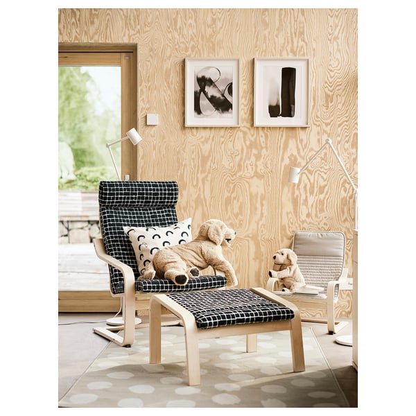 Living room with two wooden chairs, each with a stuffed animal. One has black-white, the other beige cushion. Abstract art on wooden wall, dotted rug.