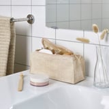 White bathroom counter with accessories: jar, toothbrush, basket, flowers, toothbrush.