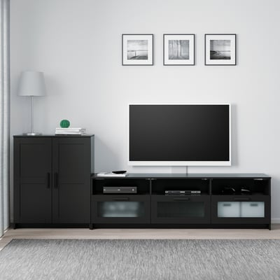 Modern black BRIMNES tv setup with cabinet and bench, sleek design, flat screen tv atop, drawers for storage, lamp, and framed photos.