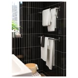 Modern bathroom with black tiled walls, two towel racks with white towels, wooden stool, plant, and sink.
