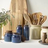 Kitchen scene with BRUGDHAJ blue jars, wooden utensils, and green crock; jars small to medium, natural decor.