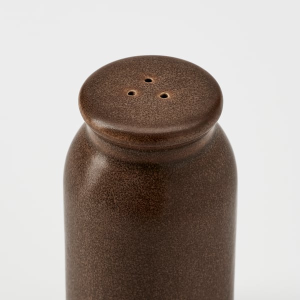 Rustic, brown stoneware spice jar with a flat lid featuring small holes for dispensing spices, standing upright.
