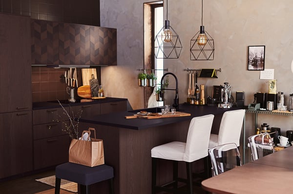 Kitchen with dark wood, pendant lamps over white island chairs.