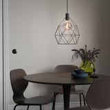 Modern dining setup with BRUNSTA lamp, small dark table, wooden chairs, green vase with flowers, and blue plates.