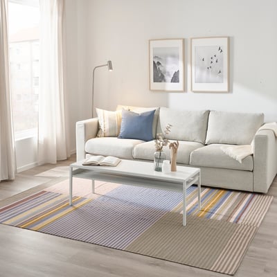 Modern living room with grey rug under sofa, colorful stripes, and contrasting art.