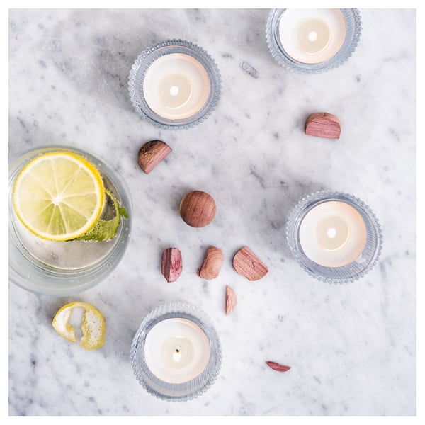 Four lit blue candles, one with a lemon slice, on white marble surrounded by small wooden pieces.