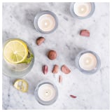 Four lit blue candles, one with a lemon slice, on white marble surrounded by small wooden pieces.
