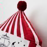 Red and white striped pillow with pompom, featuring circus design.