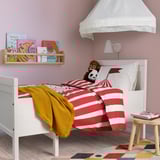 Colorful kids room with BUSENKEL red & white striped bedding, monkey plush, books, yellow throw, wooden stool, pastel rug, white walls & canopy.
