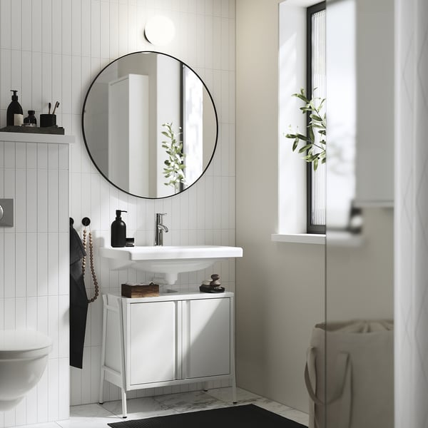 Modern bathroom with BYASJÖN white gloss cabinet under sink, round mirror, and plants. Small, sleek design amid white tiles.