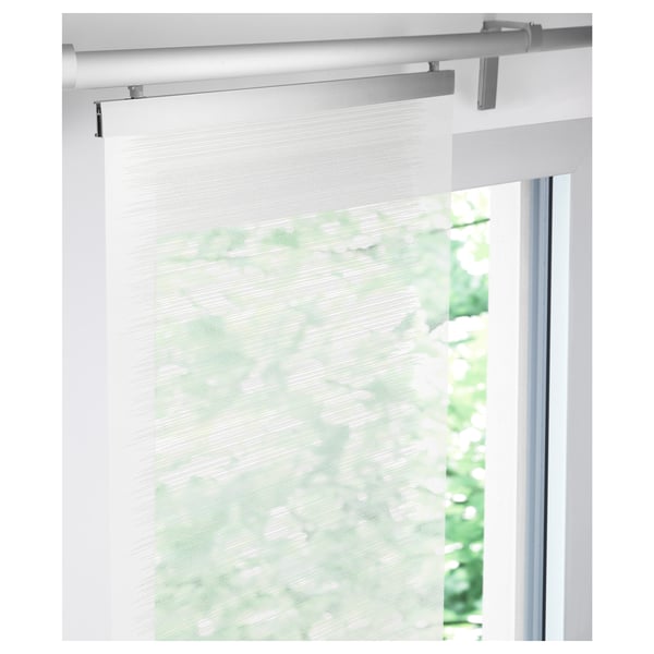 A sheer white panel curtain, mounted on brackets, softens light in a window, offering a clean, layered look.