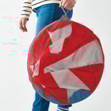 Person holding a large red mesh circle with white fabric inside, likely a childrens play tent.