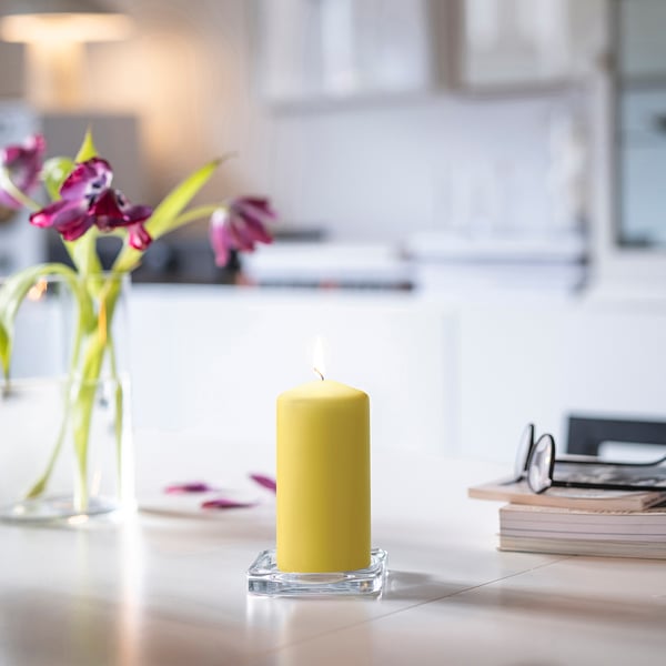 Yellow DAGLIGEN candle in glass holder near pink flowers and books.