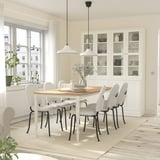 Modern white 6-seat dining set with wood table, steel legs, cushioned chairs, and glass cabinet in bright room.