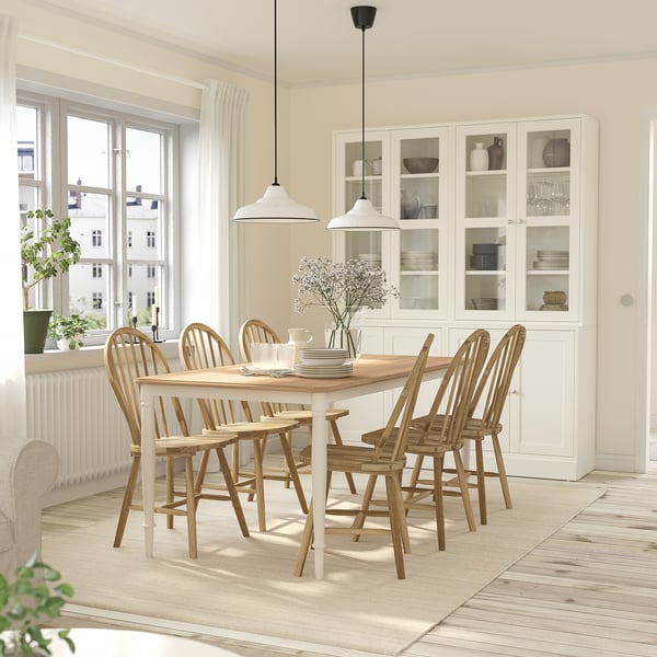 Modern dining set with 6 acacia chairs around a wooden table, vase centerpiece in a minimalist room with natural light.