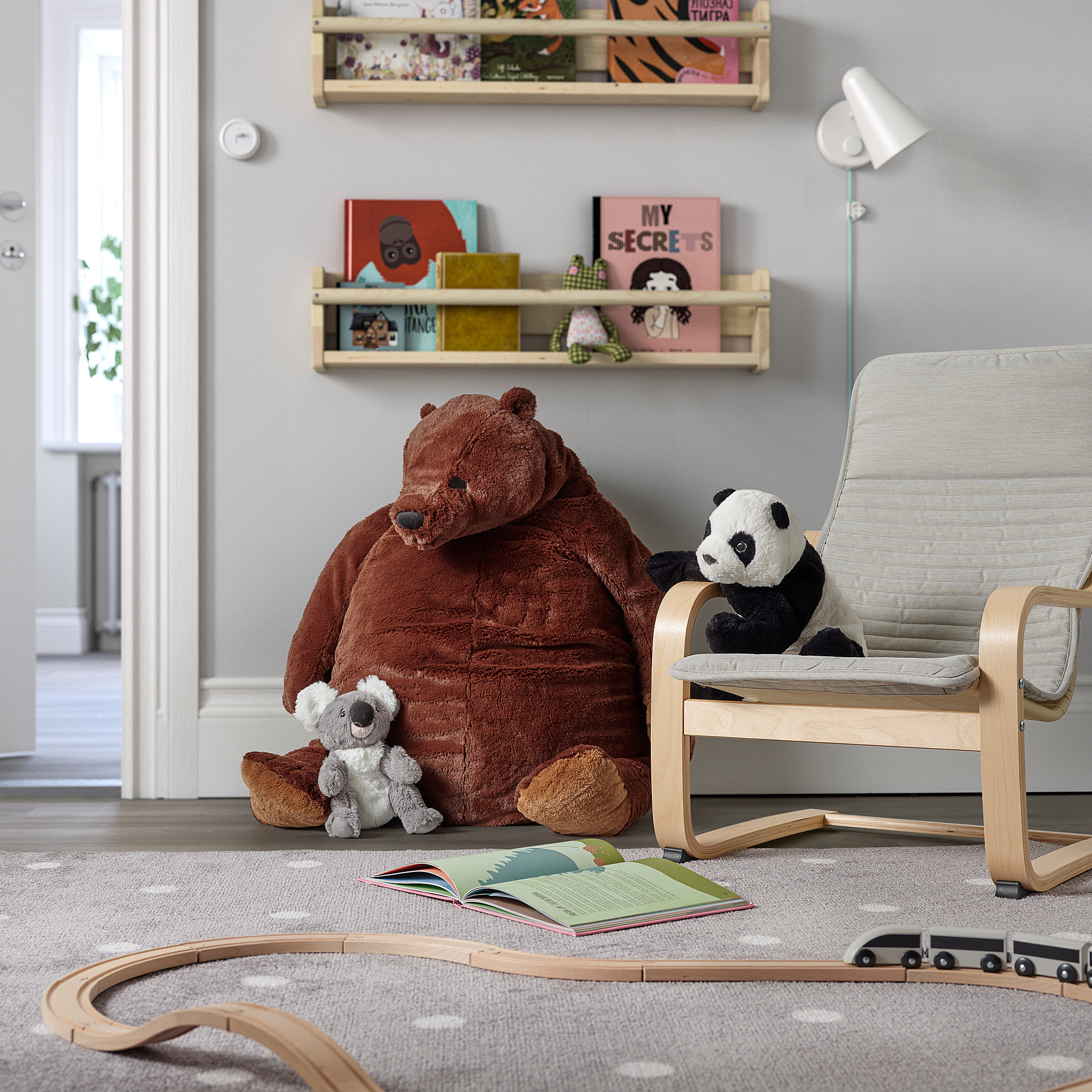 Brown bear toy by bookshelf with panda, chair, book, and train set.