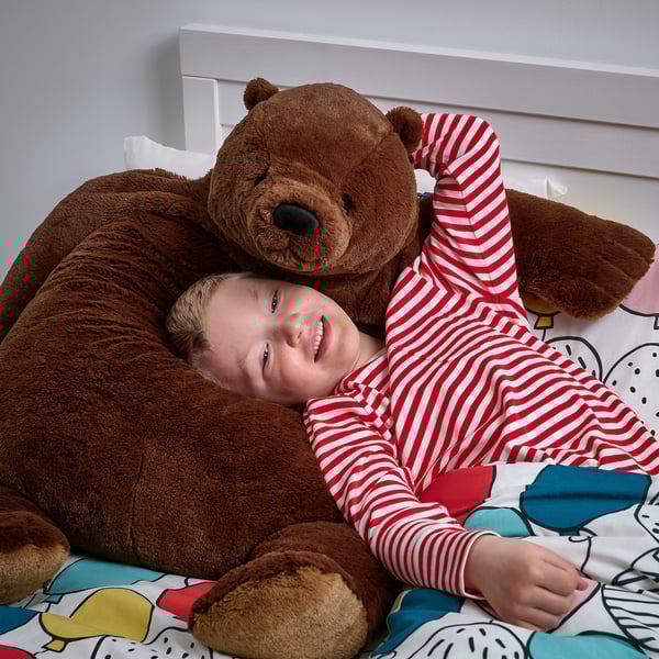 Child in striped pajamas hugs large brown teddy bear on bed.