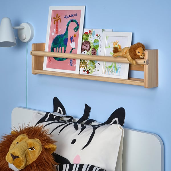 Kids room with blue walls, DJUNGELSKOG lion on bed with zebra pillow, shelf with drawings and lion toy.