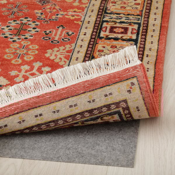 Vibrant, hand-knotted area rug with floral patterns on wooden floor, backed by non-slip mat.