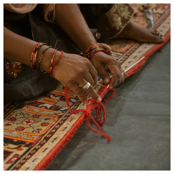 Person weaving colorful rug, focusing on patterns with needle and thread, wearing bracelets.
