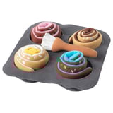 A toy baking tray with four fabric buns, each with different colorful designs and a brush on top.