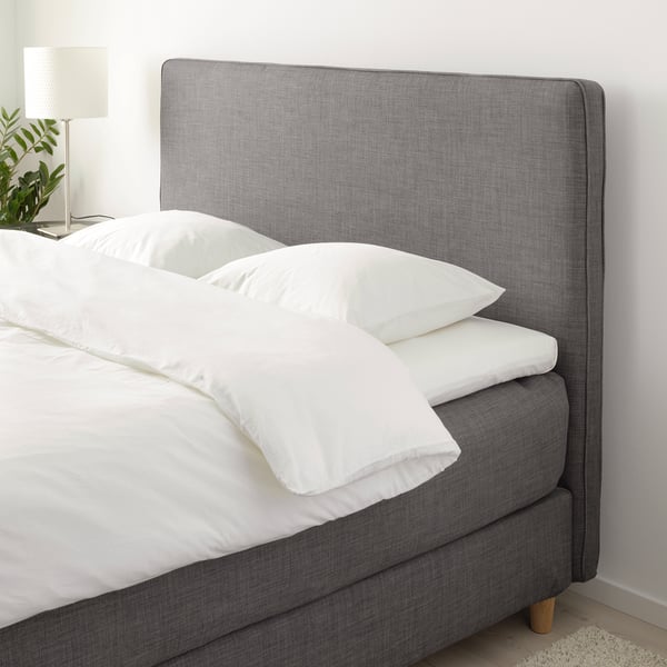 Cozy bed with soft gray headboard, white pillows, and lamp. Comfortable for reading.