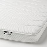 A close-up of an IKEA DUNVIK mattress, showcasing its textured white surface and embroidered logo, highlighting its quality and design.