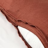 Close-up of rust-colored cushion covers zipper, revealing white inner cushion, illustrating removable design.