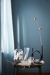Clear glass hourglass with tinted finish, modern design, stands on metal stand, minimalist decor, blue wall background.