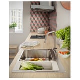 Modern kitchen with stainless steel sink, filled with washed veggies. Wood counter, colorful tile backsplash.