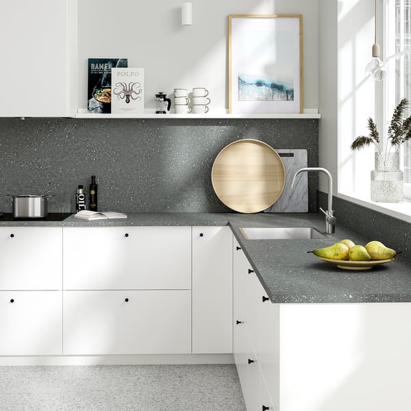 Modern kitchen with gray countertop, white cabinets, sink, and natural decor.