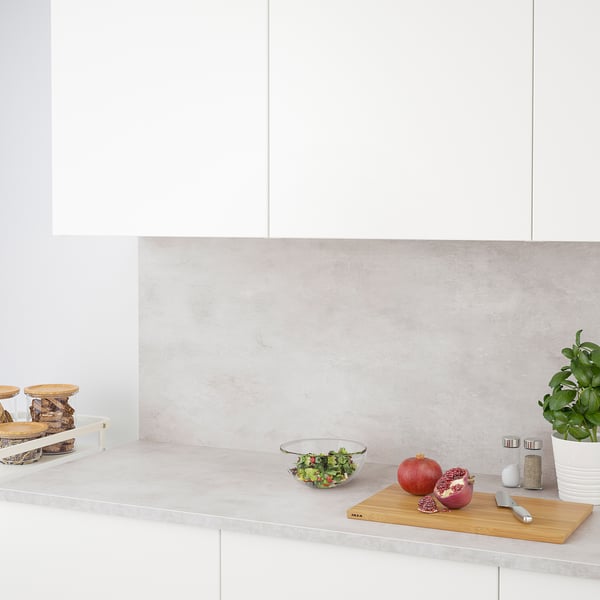 Modern kitchen counter with a bowl of salad, cutting board, pomegranates, and plant; part of the EKBACKEN worktop series.