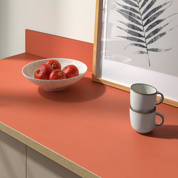A kitchen countertop with a bowl of pomegranates and stacked mugs, ideal for easy cleaning and maintenance, with a 25-year guarantee.