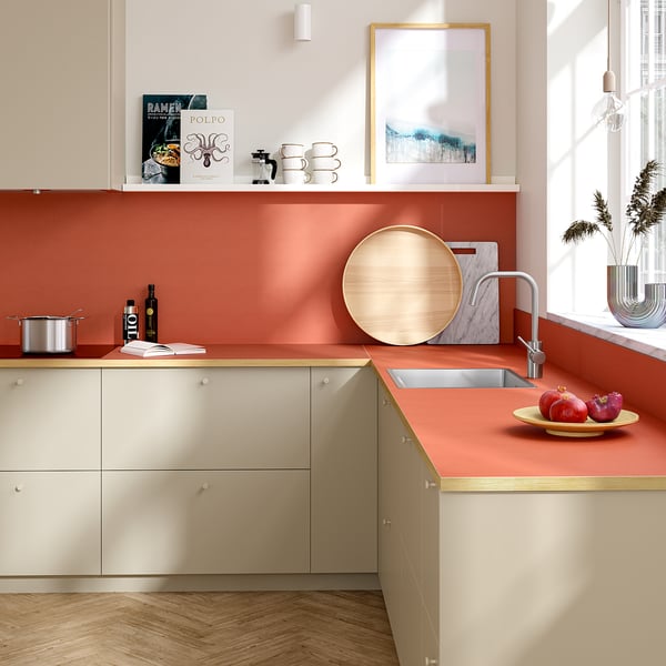 Modern kitchen with terracotta countertop, sink, wooden tray, and pomegranates. Beige cabinets, light floors, white walls.
