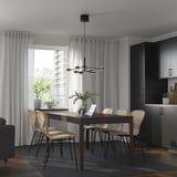 Modern dining setup with wooden EKEDALEN table, chairs, and laptop. Large window with light curtains. Room is spacious and minimalist.