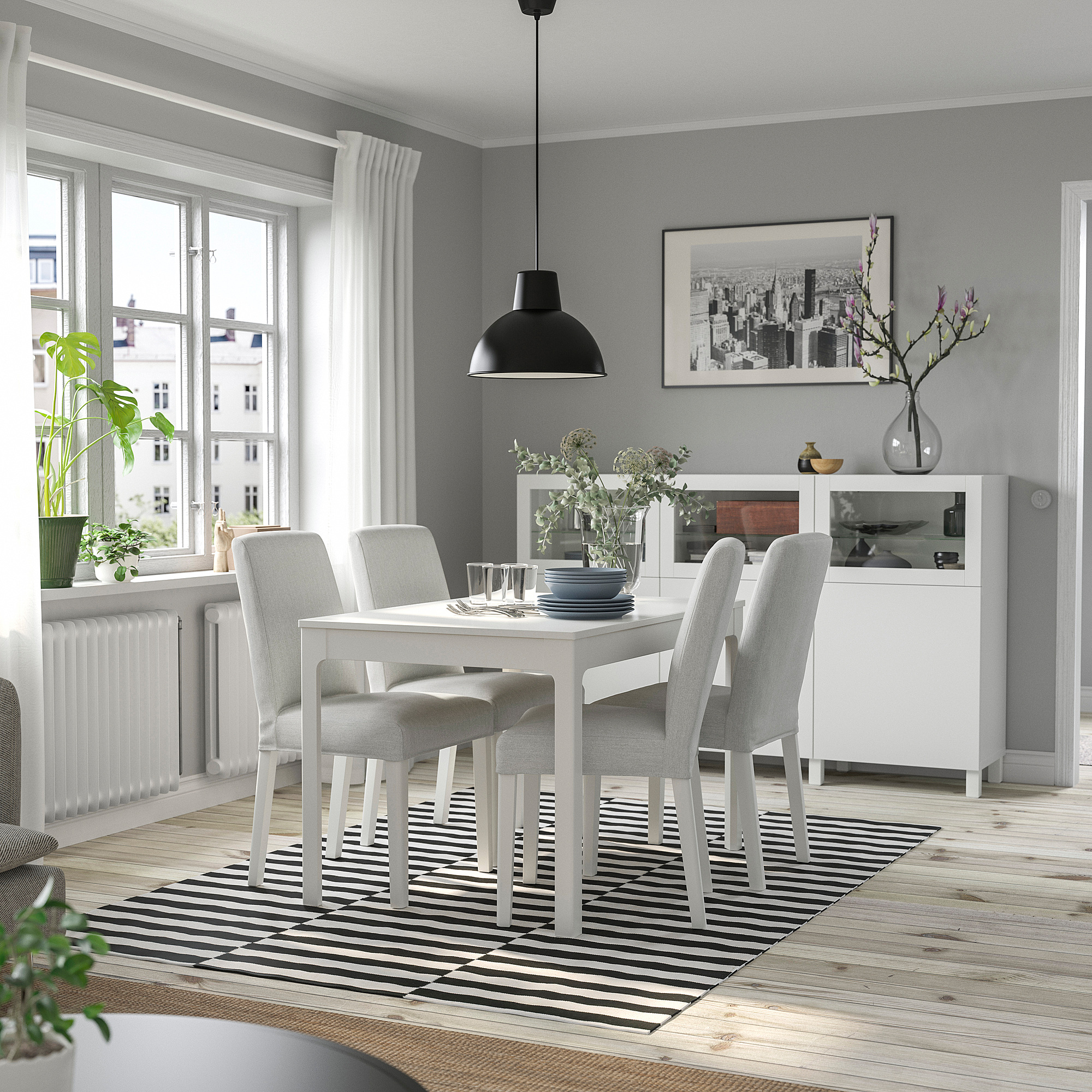 Modern dining room with white EKEDALEN table, gray chairs, plant, dishes, striped rug, lamp, and framed photo.