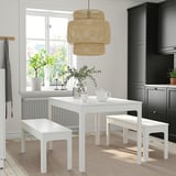Minimalist dining set with extendable white table, wicker light, and simple decor in a bright kitchen.